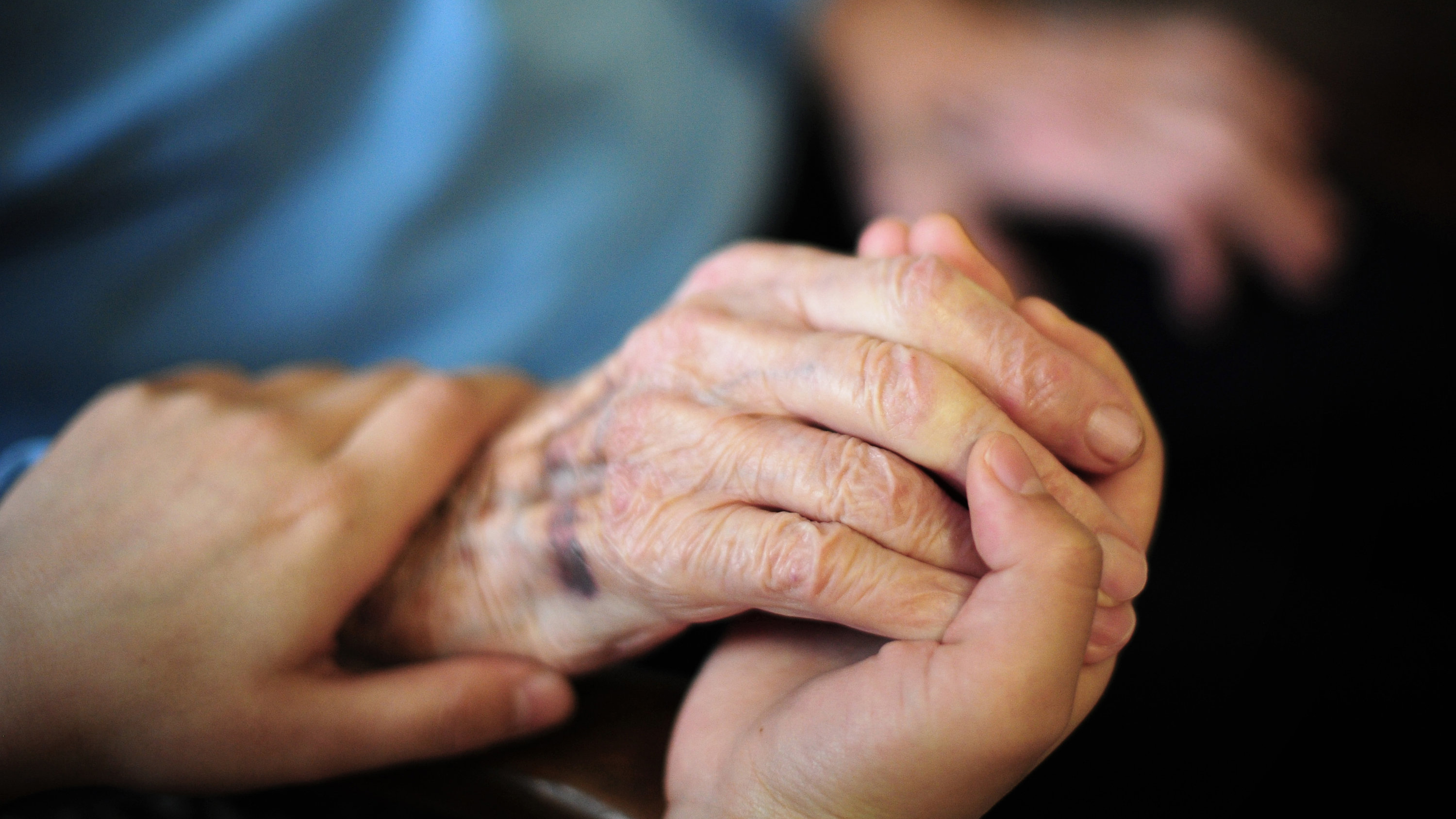 Eine Pflegekraft streichelt die Hand eines Senioren. | dpa