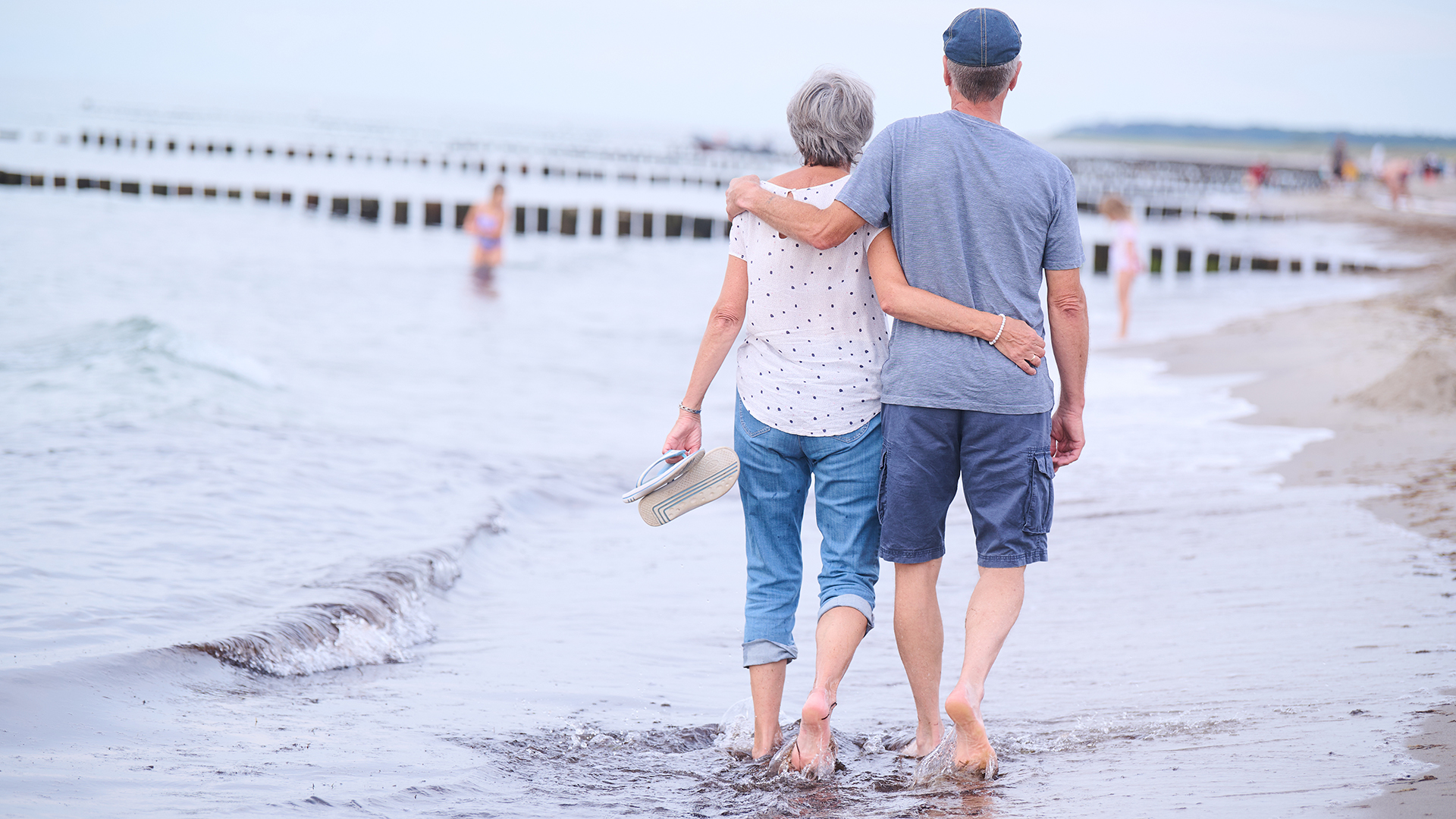Ein Rentnerehepaar geht am Strand Arm in Arm spazieren. | picture alliance/dpa