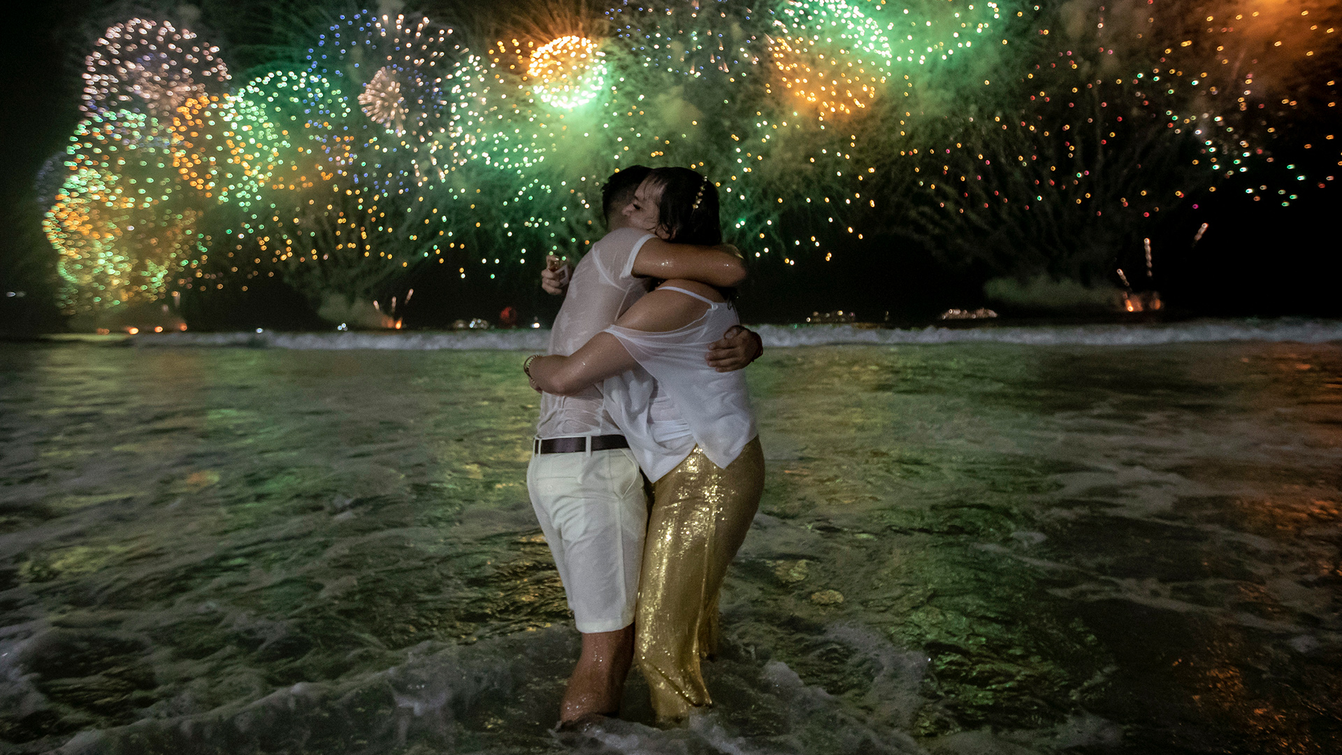Ein Paar umarmt sich im Wasser stehend, im Hintergrund Feuerwerk | dpa