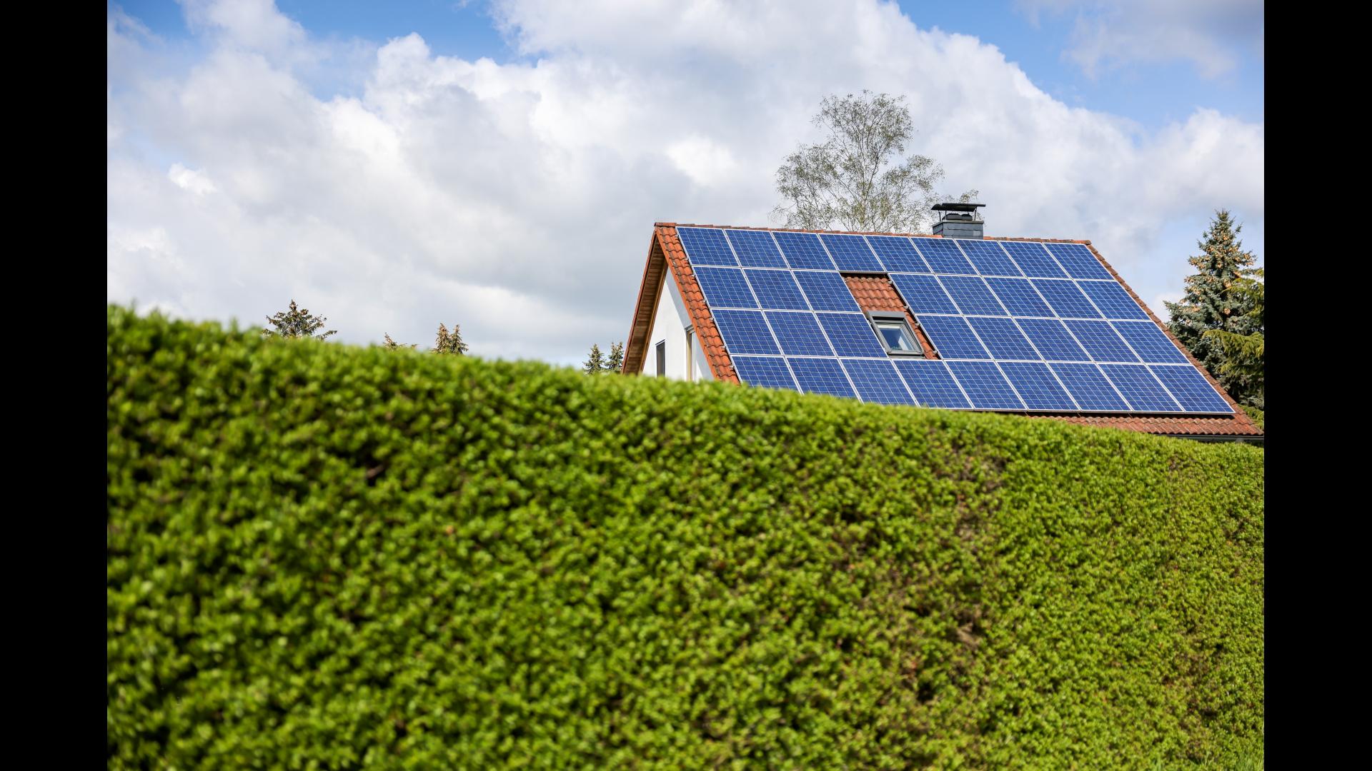 Ein Einfamilienhaus mit Solarzellen auf dem Hausdach steht hinter einer grünen Hecke. | dpa