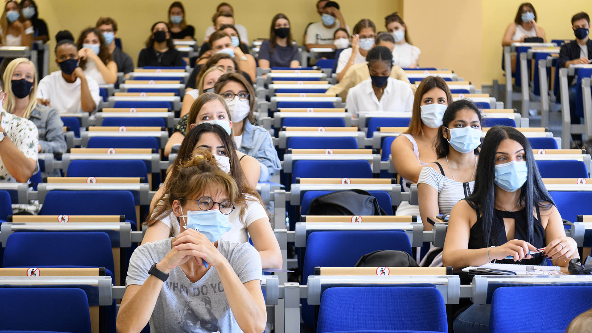Studentinnen und Studenten mit Mund-Nasen-Schutz sitzen während eines Kurses in einem Hörsaal in der Juristischen Fakultät der Universität Neuenburg. | picture alliance/dpa/KEYSTONE