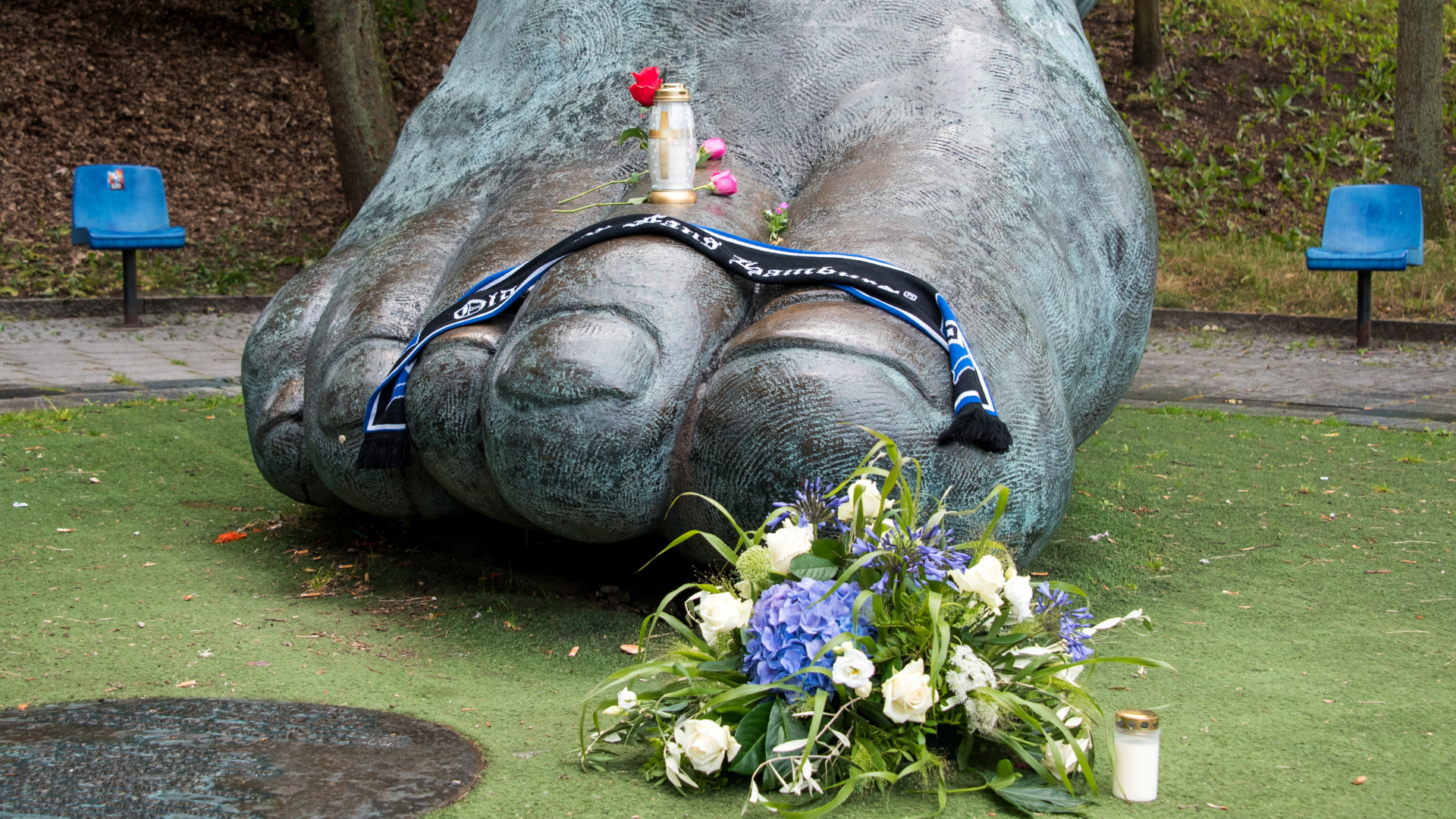 Auf einer Bronze vor dem Volksparkstadion, die den Fuß des ehemaligen Fußballspielers Uwe Seeler darstellen soll, stehen und liegen eine Kerze, Blumen und ein Schal. | dpa