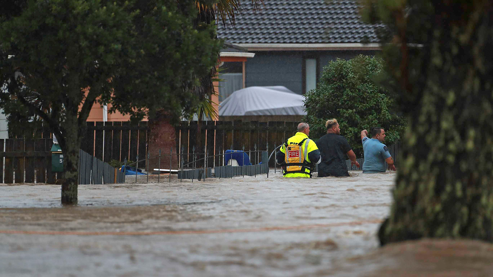 Rettungskräfte und ein Mann waten durch das Hochwasser einer überschwemmten Straße in Auckland, Neuseeland.  | dpa