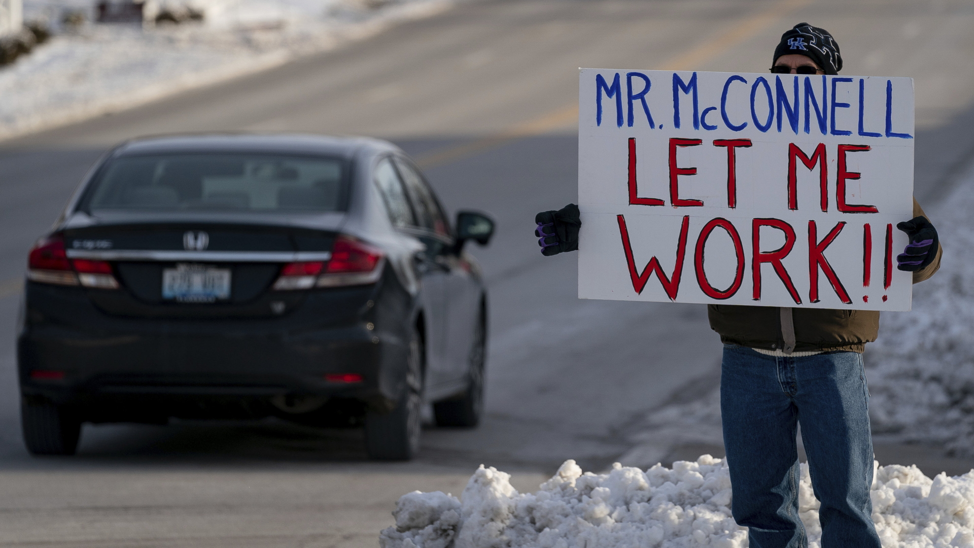Ein Beamter steht mit einem Plakat an einer Straße in den USA - er fordert den republikanischen Abgeordneten McConnell auf, ihn wieder arbeiten zu lassen und den Shutdown zu beenden. | AP