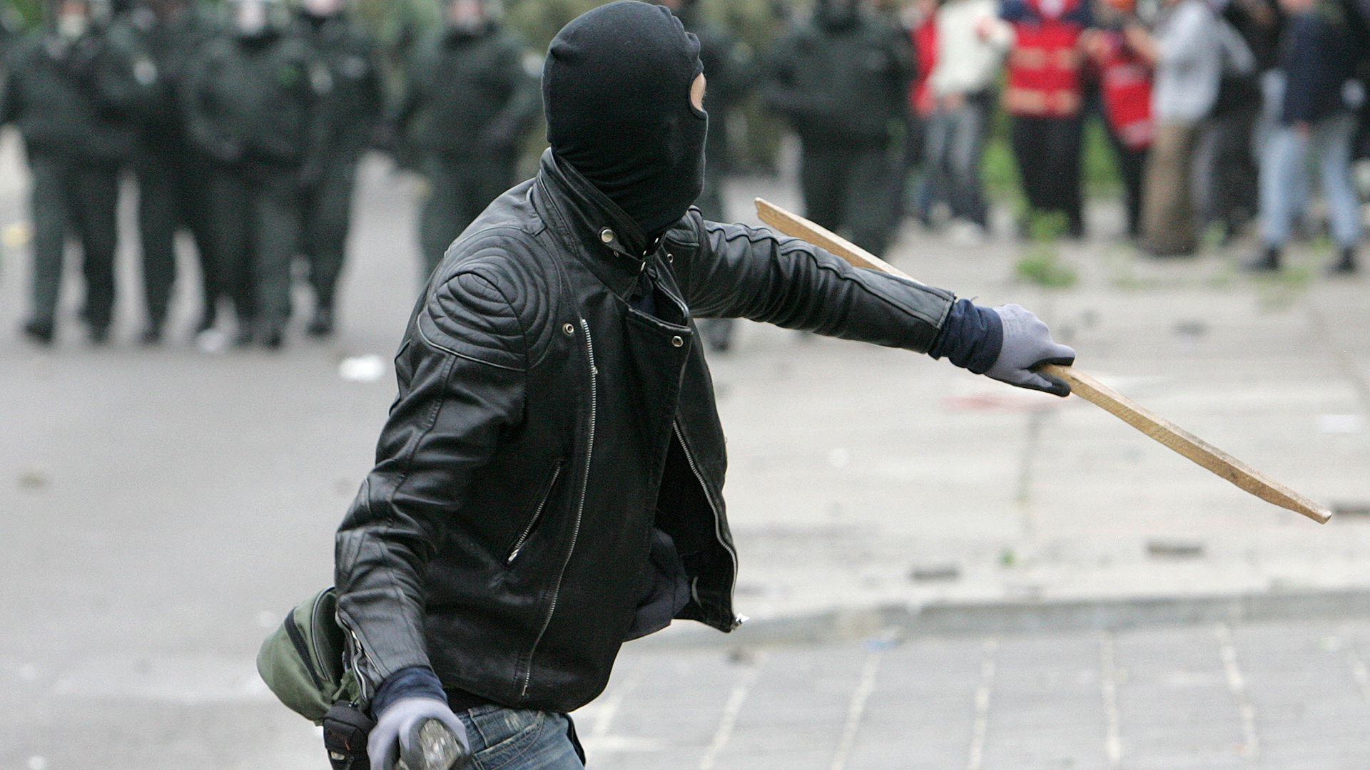 Ein vermummter Demonstrant wirft einen Stein in Richtung Polizei. | picture alliance / ASSOCIATED PR