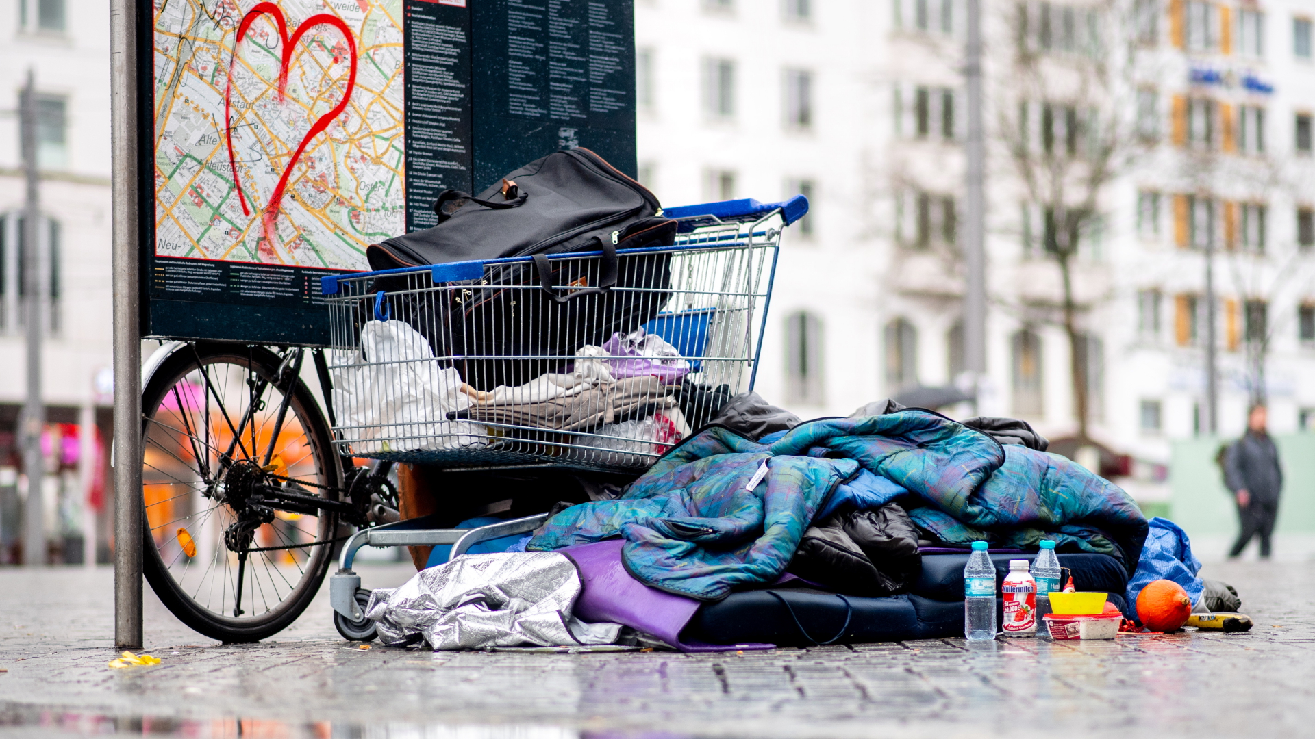 Ein Schlafsack und Kleidungsstücke liegen vor einem Einkaufswagen auf Pflastersteinen.  | dpa
