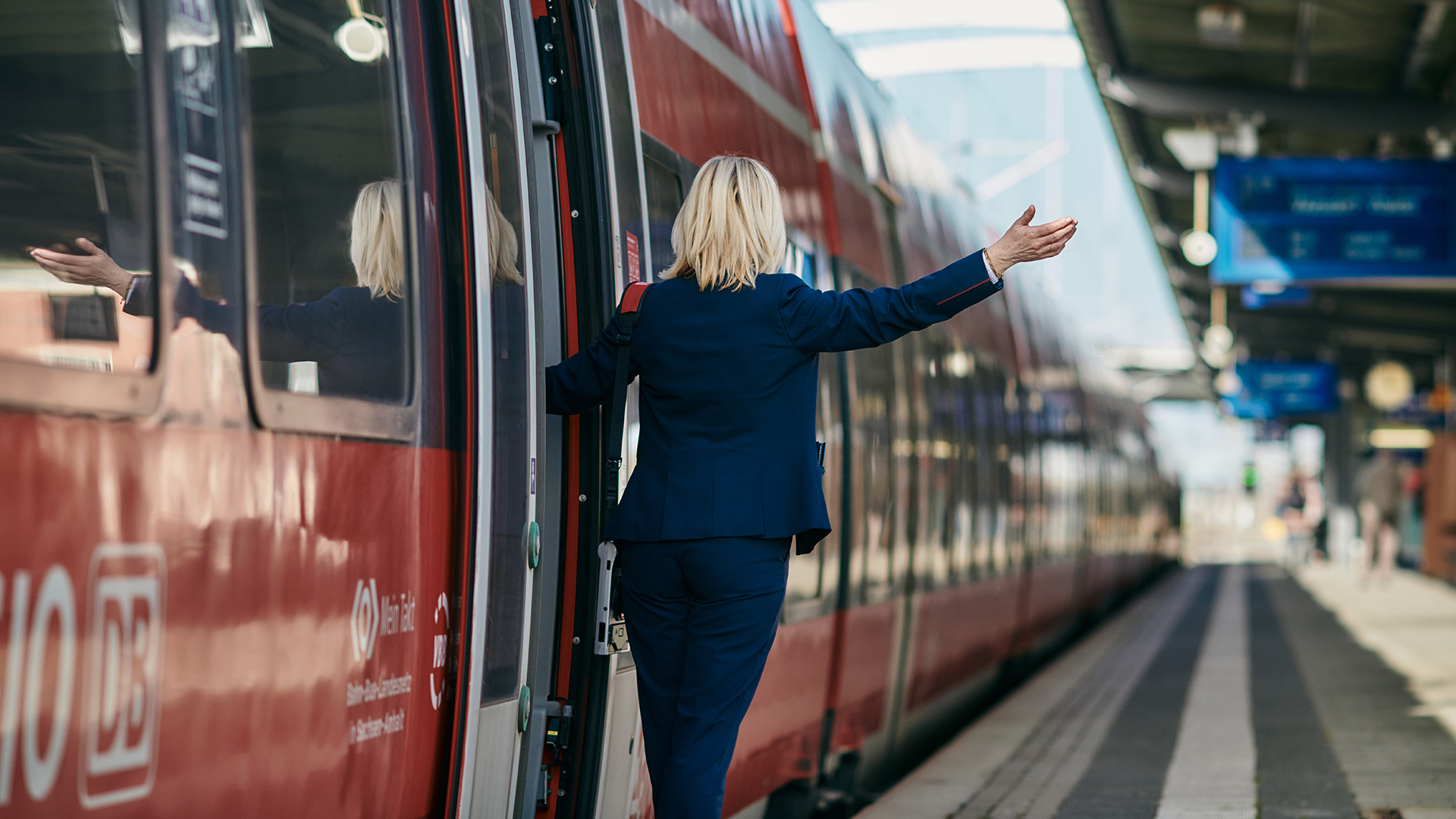 Eine Zugbegleiterin am Bahnsteig winkt zur Abfahrt. | Deutsche Bahn AG / Dominic Dupont